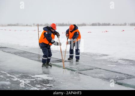 Les employés radeau des blocs de glace le long d'une chaîne coupée un lac gelé Banque D'Images