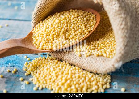 Millet jaune cru dans une cuillère en bois sur toile de toile de toile de burap sur un fond de planches rustiques bleues. Gros plan. Banque D'Images