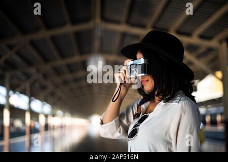 Les cheveux ondulés femme en chemise blanche et chapeau noir prenez une photo d'une main tout en se tenant dans le couloir de la plate-forme du train. Banque D'Images