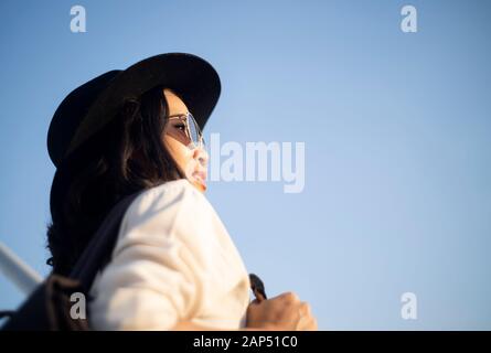 Wavy woman in black hat et lunettes de soleil sur le toit à regarder la vue du lever de bonheur et de joie. Banque D'Images