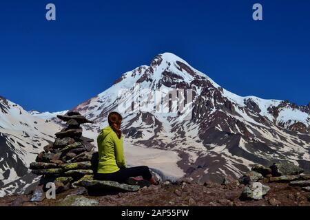 Une jeune fille en sweat-shirt jaune se trouve à côté d'un homme en pierre et regarde le sommet de la montagne Kazbek couverte de glacier. Belle journée ensoleillée haute Banque D'Images
