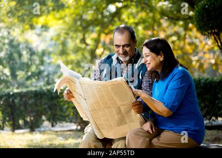 Heureux couple senior lecture journal à l'extérieur au parc Banque D'Images