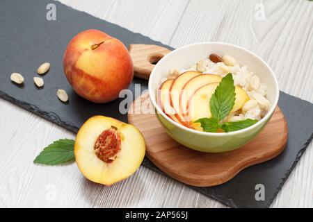 La bouillie de sorgho avec des morceaux de pêche, de noix et d'amande douce, Bol en porcelaine de peach sur cartes en bois et en pierre et fond gris. Glu Vegan Banque D'Images