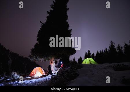 L'homme est assis près d'une tente la nuit en hiver dans les montagnes Banque D'Images