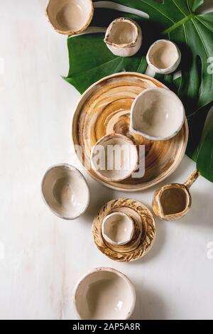 Variété de différents plats en céramique vide, bols, pichets et plateaux sur feuilles de monstera exotiques sur fond blanc en arrière-plan. Mise à plat, de l'espace Banque D'Images