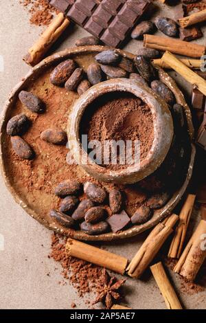 Barre de chocolat noir et au lait entier et coupé avec des fèves de cacao, poudre de cacao et des bâtons de cannelle sur brown texture background. Mise à plat, de l'espace Banque D'Images