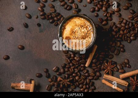 Espresso Café noir avec mousse en céramique noire, avec soucoupe, épices et fèves grillées au-dessus plus de brown texture background. Mise à plat, de l'espace Banque D'Images