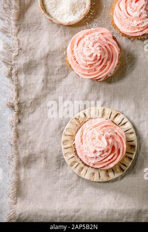 Petits gâteaux faits maison avec crème au beurre rose flocons de noix de coco et servi sur une plaque en céramique sur toile gris en arrière-plan. Mise à plat, de l'espace Banque D'Images