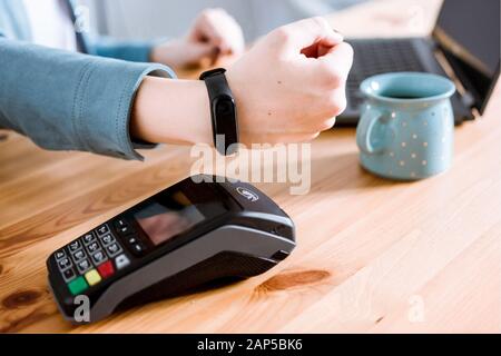 Femme travaillant sur un ordinateur portable, utilisant un terminal pour le paiement sans contact via Smartwatch pour sa commande dans un café. Nouvelle technologie de paiement NFC Banque D'Images