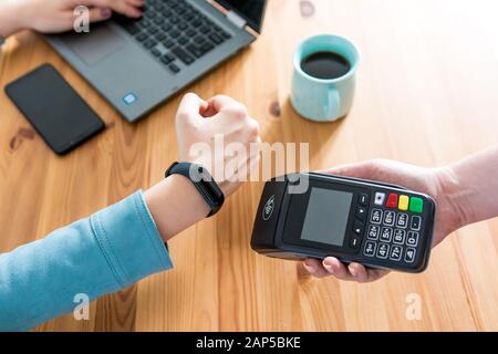 Femme travaillant sur un ordinateur portable, utilisant un terminal pour le paiement sans contact via Smartwatch pour sa commande dans un café. Nouvelle technologie de paiement NFC Banque D'Images