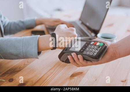 Femme travaillant sur un ordinateur portable, utilisant un terminal pour le paiement sans contact via Smartwatch pour sa commande dans un café. Nouvelle technologie de paiement NFC Banque D'Images