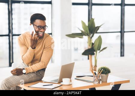 Étudiant africain parlant sur le téléphone portable assis sur le bureau Banque D'Images