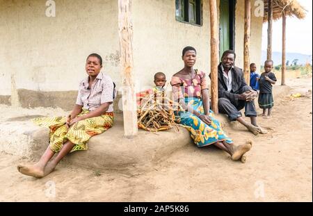 Trois générations d'une famille malawienne s'assoient sur la marche de leur hutte de boue dans un village Banque D'Images