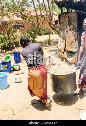 Un portrait de deux femmes malawiennes portent un pot en métal très lourd de porridge de maïs vapeur dans un cadre de village Banque D'Images