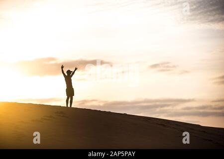 Jeune homme levant ses bras haut dans une victoire ou un geste de liberté. Silhouette imreconnaissable. Banque D'Images