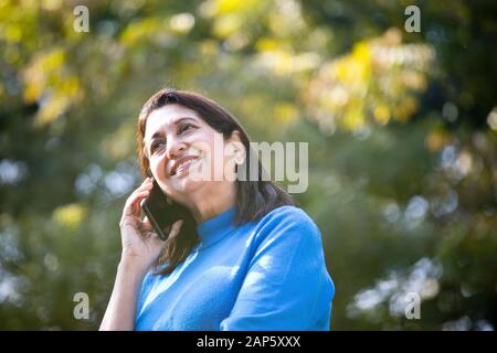 Heureuse femme senior utilisant le téléphone au parc Banque D'Images