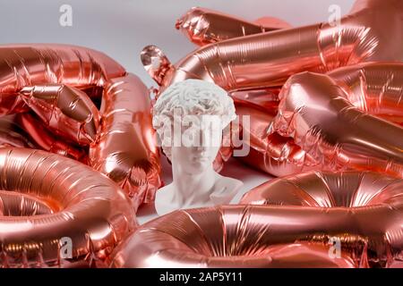 Statue de gypse de la tête de David. Statue du David de Michel-Ange copie en plâtre rose parmi les ballons d'or aluminium Banque D'Images