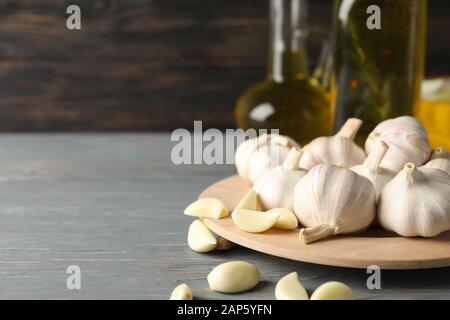 Assiette de l'ail, de tranches, de l'huile sur table gris contre fond de bois, de l'espace pour le texte. Libre Banque D'Images