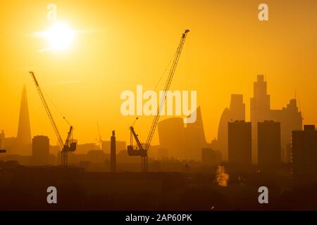 Le soleil se couche derrière les grues à tour et la ville de Londres, y compris le tesson (à gauche) et de gratte-ciel dans le quartier financier de la ville de Londres. Banque D'Images