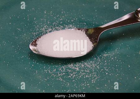 Concept de comptage des calories : gros plan d'une cuillère d'argent isolée remplie de sucre blanc sur un vieux plat de porcelaine rayé bleu Banque D'Images