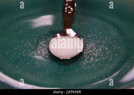 Concept de comptage des calories : gros plan d'une cuillère d'argent isolée remplie de sucre blanc sur un vieux plat de porcelaine rayé bleu Banque D'Images