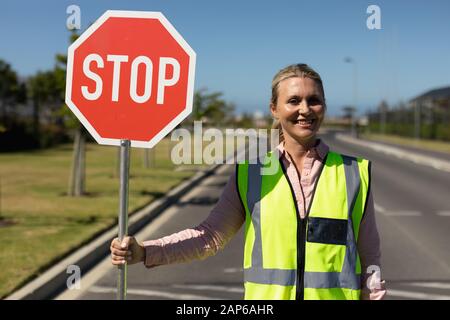 Femme portant un gilet haute visibilité et tenant un panneau stop Banque D'Images