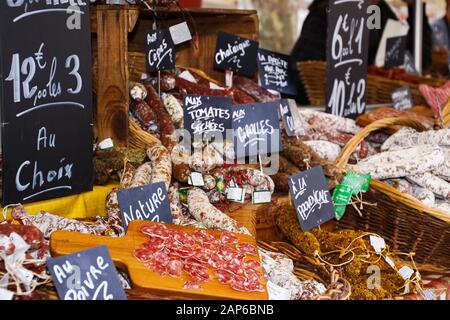 Différents types de salami provocale français présentés dans des paniers en osier avec des planches à craie manuscrites sur le marché fermier - Saint-Tropez, France Banque D'Images