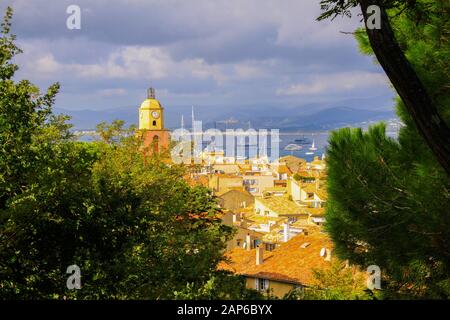 Vue aérienne au-delà des arbres sur le village méditerranéen avec tour d'église et fond de mer le jour nuageux - Saint-Tropez, Côte d'Azur, France Banque D'Images