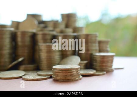 Une grande quantité de pièces de monnaie ukrainienne brillante de 1 hryvnia s'empile sur une table en bois sur fond d'arbres verts flous. Le concept d'affaires et riche l Banque D'Images