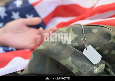 Perles militaires argentées avec étiquette de chien et main de soldat mort sur le drapeau de tissu des États-Unis et uniforme de camouflage. Tué dans l'unité d'action. Jour commémoratif Banque D'Images