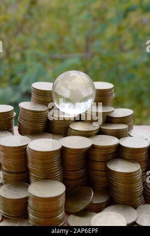 Planète en verre sur une grande pile de pièces de monnaie ukrainienne brillante 1 hryvnia s'empare sur fond d'arbres verts flous. Le concept de transfert d'argent autour Banque D'Images