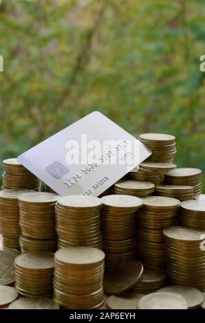 Carte de crédit sur grande pile de pièces de monnaie ukrainienne brillant 1 hryvnia pile gros sur fond d'arbres verts flous. Le concept de transfert d'argent et onl Banque D'Images