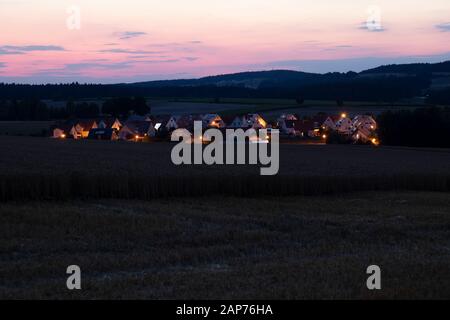 un petit village allemand derrière un champ de maïs au milieu de la nature pendant le coucher du soleil à l'heure bleue Banque D'Images