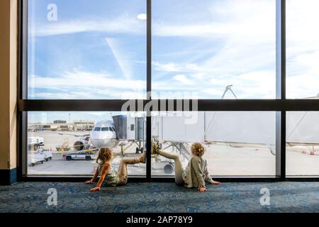 deux filles assises sur le sol à l'aéroport, regardant un avion qui attend Banque D'Images