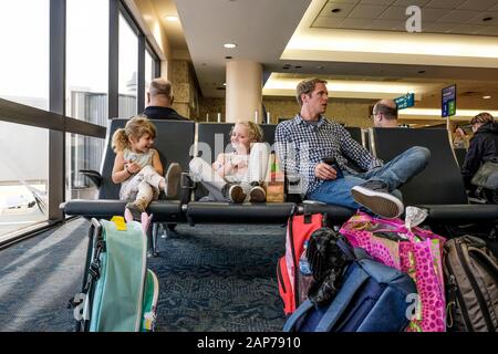 deux filles et un père assis dans le terminal de l'aéroport attendent de rire Banque D'Images