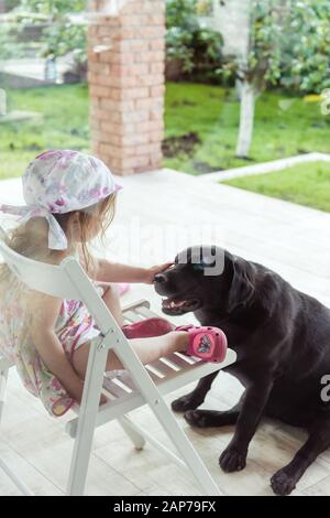 Petite fille qui a fait le chasse à un grand chien Labrador retriever noir Banque D'Images