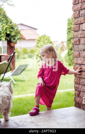 Une petite fille dans la cour jouant avec un chien blanc mignon Banque D'Images