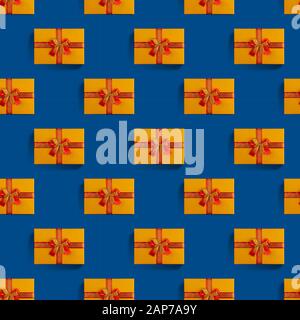 Boîte cadeau orange sans couture avec ruban doré et rouge sur fond bleu classique. Noël vacances, fête des valentines et concept d'anniversaire. Banque D'Images