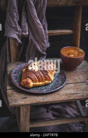 Croissant aux amandes et tasse de café servis sur une ancienne chaise en bois rustique Banque D'Images