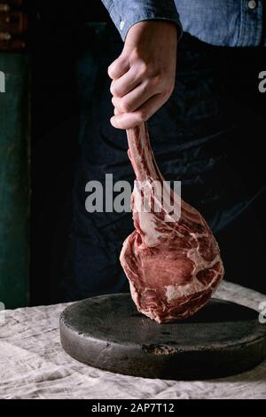 Man's hands holding non cuites brutes tomahawk boeuf Black Angus Steak sur les os sur le linge de table cloth. Style rustique Banque D'Images