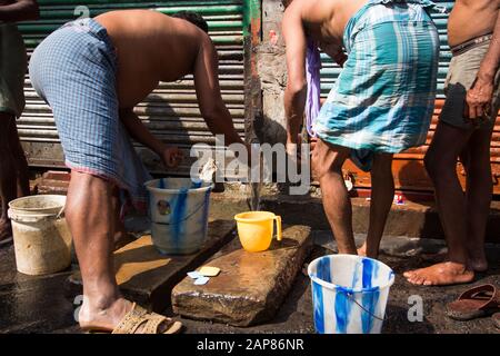 Les hommes et les garçons sont occupés à se baigner et à nettoyer dans la rue. Les conduites d'eau sont activées pour les besoins de lavage. À Kolkata (Calcutta), Inde. Banque D'Images