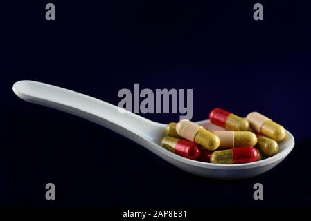Une grande cuillère blanche pour le médicament remplie de capsules et de médicaments sur fond bleu Banque D'Images