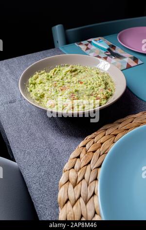 Sauce guacamole verte servie sur une plaque sur une table de tissus gris sur fond noir Banque D'Images