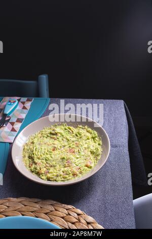 Sauce guacamole verte servie sur une plaque sur une table de tissus gris sur fond noir Banque D'Images