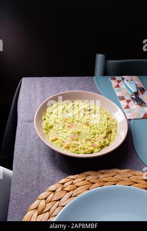 Sauce guacamole verte servie sur une plaque sur une table de tissus gris sur fond noir Banque D'Images