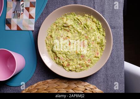 Sauce guacamole verte servie sur une plaque sur une table de tissus gris sur fond noir Banque D'Images