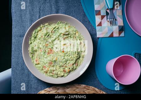 Sauce guacamole verte servie sur une plaque sur une table de tissus gris sur fond noir Banque D'Images