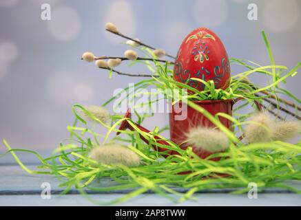 Un œuf de pâques est sur une petite arrosoir rouge comme sur un stand sur un fond flou. Banque D'Images