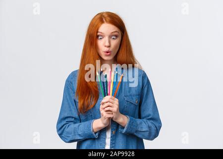 Fille avide de commencer nouveau cours d'art, apprendre à concevoir, faire des modèles, debout avec des crayons de couleur, les lèvres pliantes utilisées, regarder les outils demandé et Banque D'Images