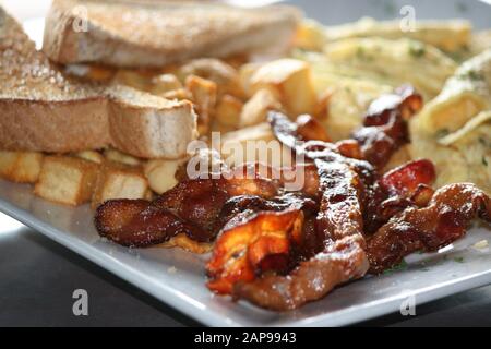 des tranches de bacon de porc croustillantes et bien cuites frites ou grillées avec des hash browns et des toasts avec des tomates sur plaque dans une vue rapprochée pour le déjeuner ou le dîner du petit déjeuner Banque D'Images